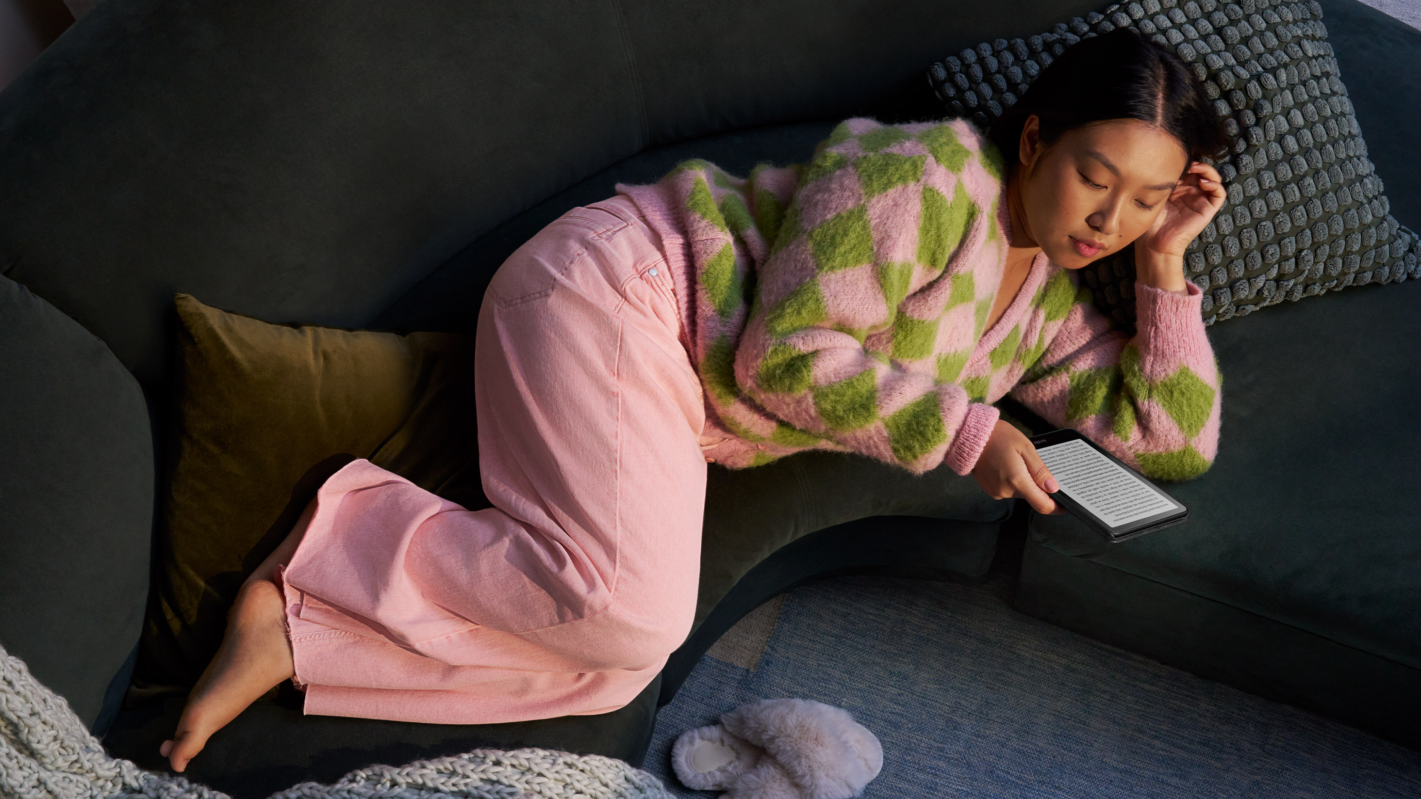 Uma mulher está deitada em um sofá enquanto lê seu Kindle Paperwhite Signature Edition.